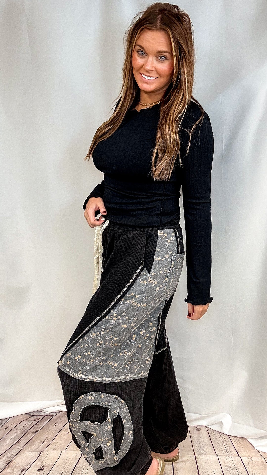 Woman wearing black long sleeve ribbed top and black pants with floral patchwork on plain background
