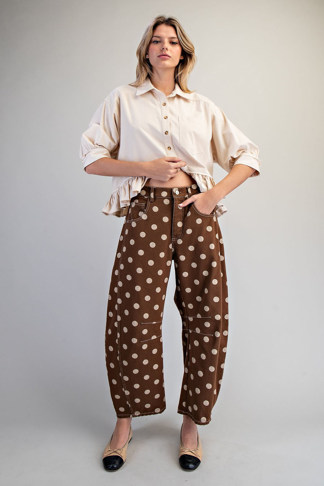 Woman wearing brown polka dot pants and beige top on plain background