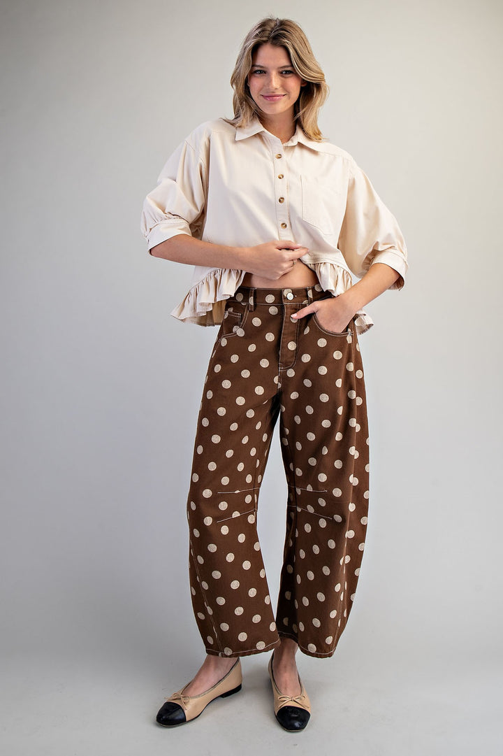 Woman wearing brown polka dot pants and beige top on plain background