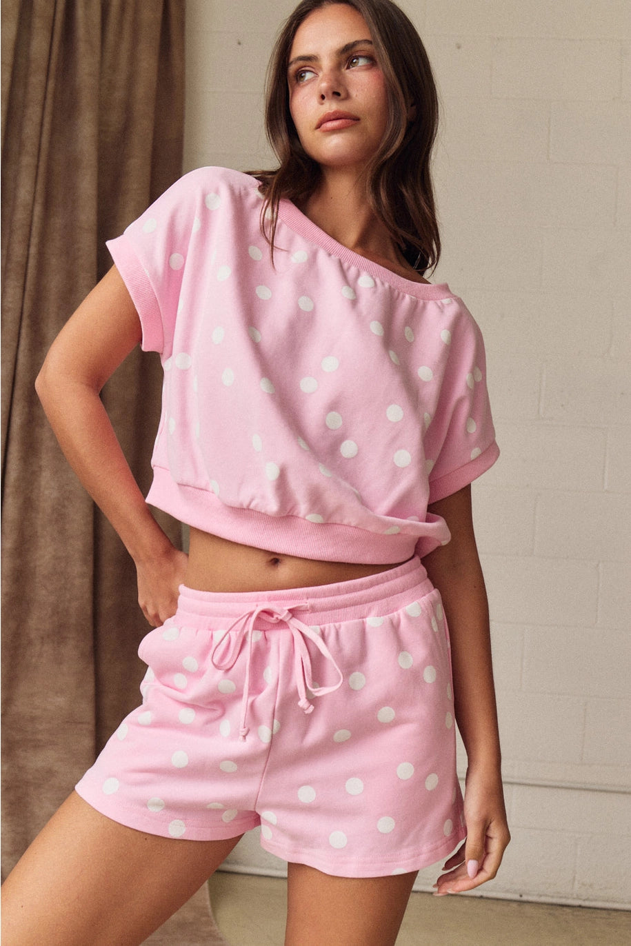 Woman wearing a pink polka dot top and shorts set against a neutral background