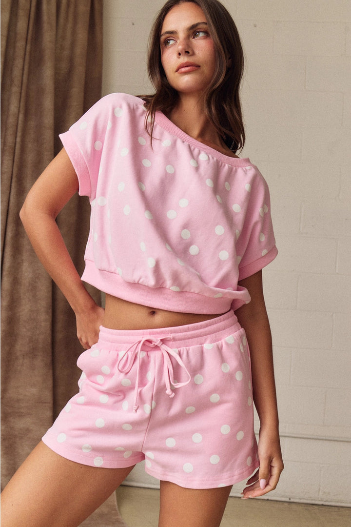 Woman wearing a pink polka dot top and shorts set against a neutral background