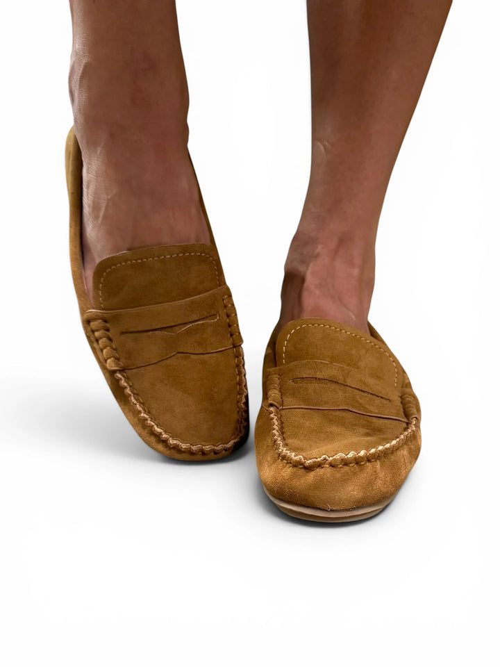 Pair of loafers in tan on a persons feet against a white background