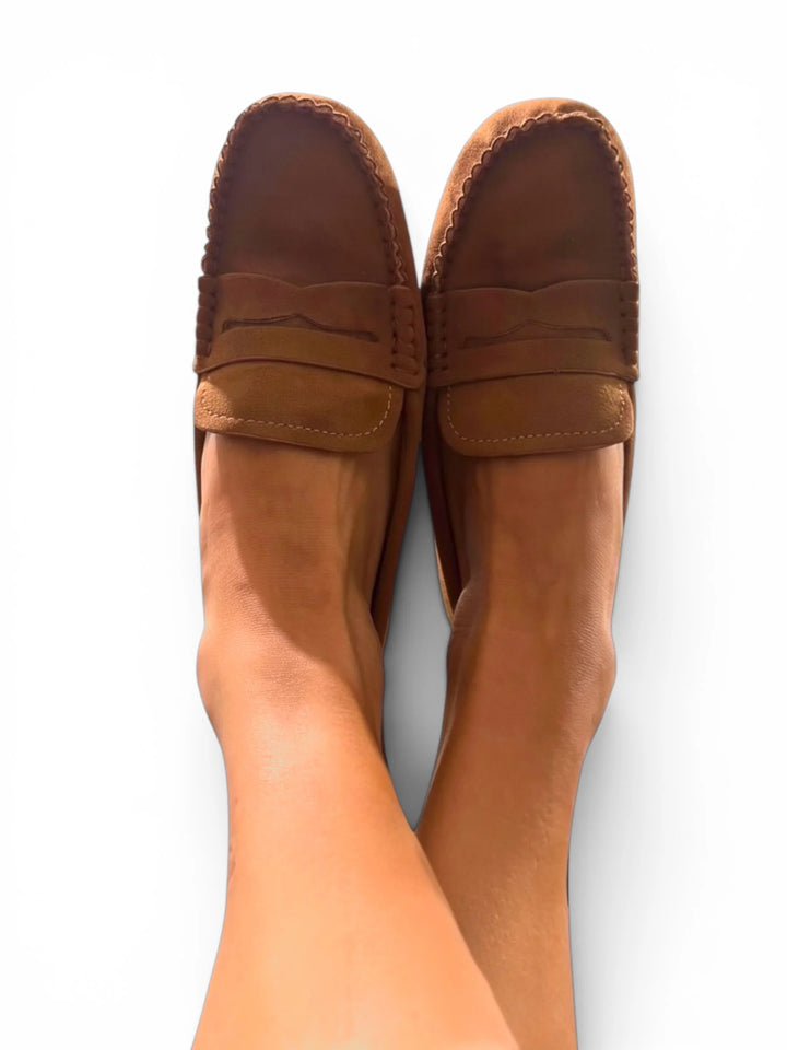 A pair of brown suede penny loafers worn on feet, shown from a top-down view against a plain white background.
