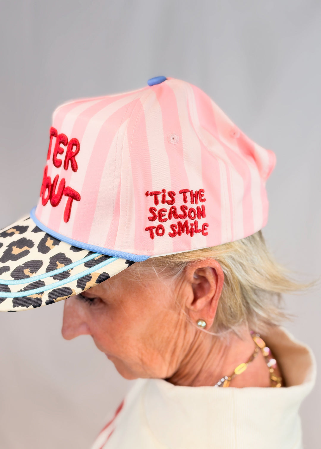 Woman shown from side view wearing pink stripe trucker hat with &