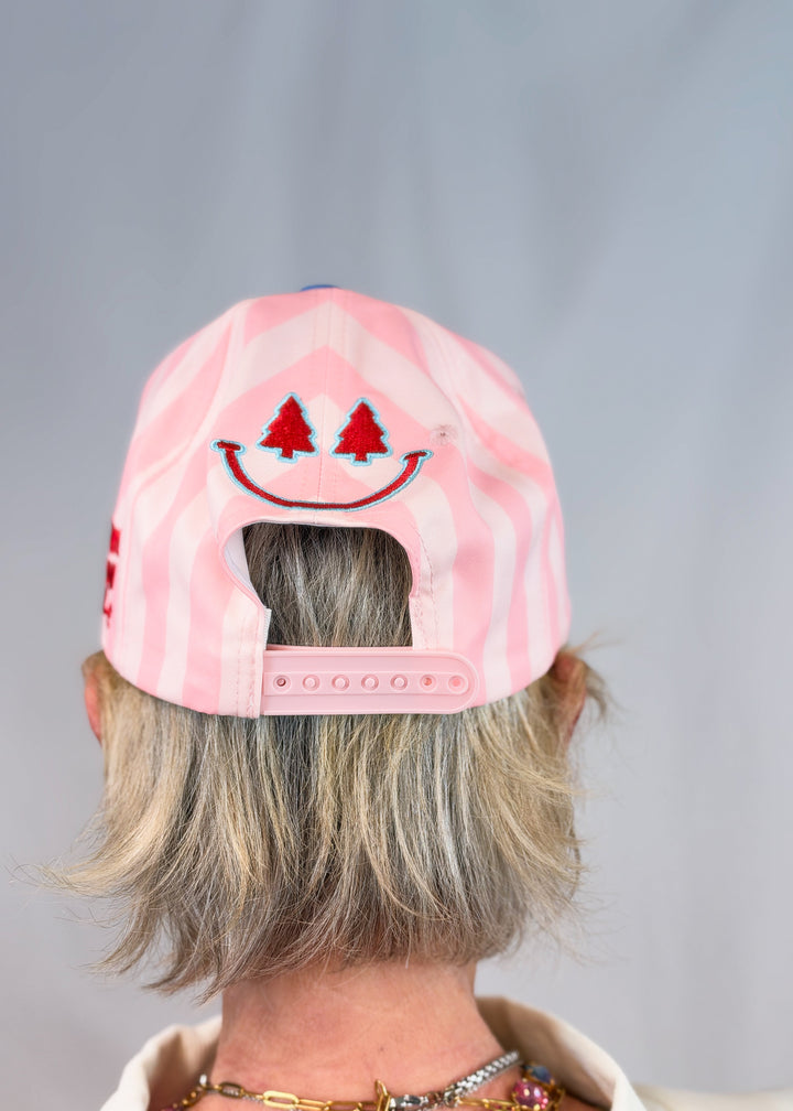Woman shown from back wearing pink stripe trucker hat with smiley face embroidered on back on plain background