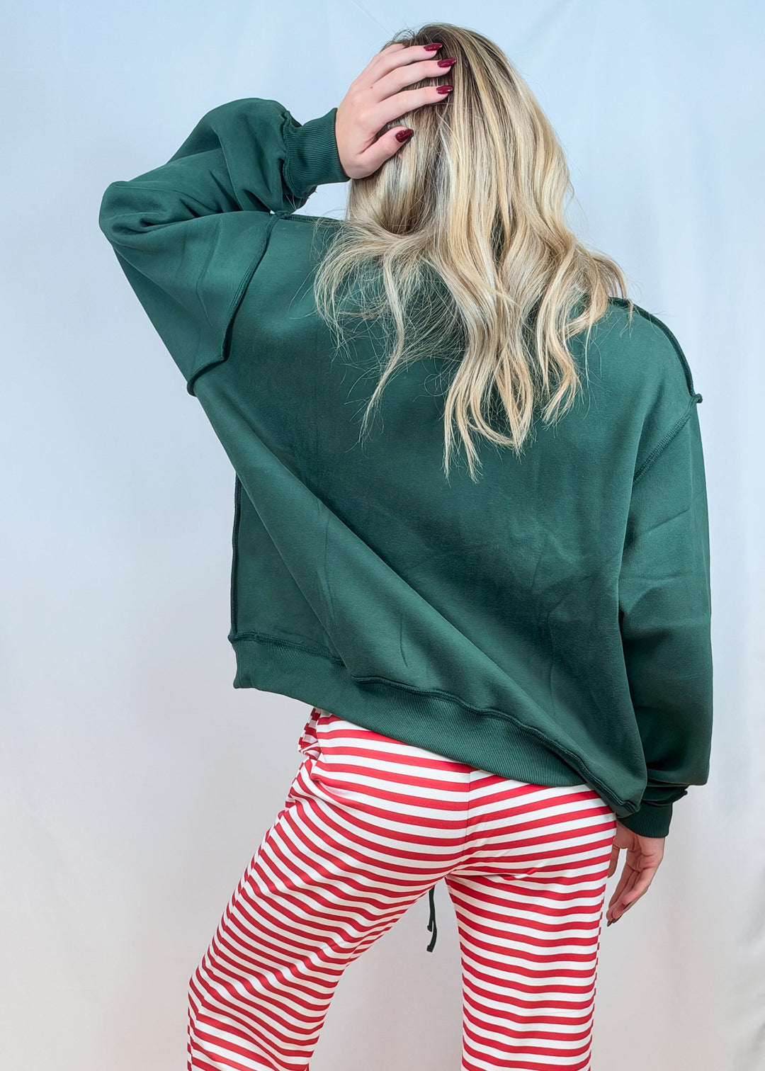 Woman shown from back wearing green sweatshirt and red and white stripe pants on plain background