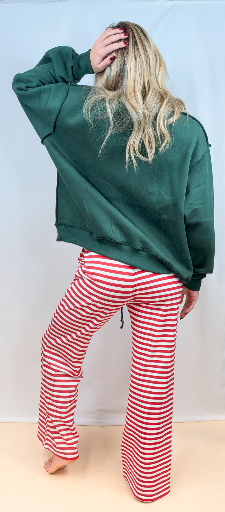 Woman shown from back view wearing green sweatshirt with red and white stripe pants on plain background
