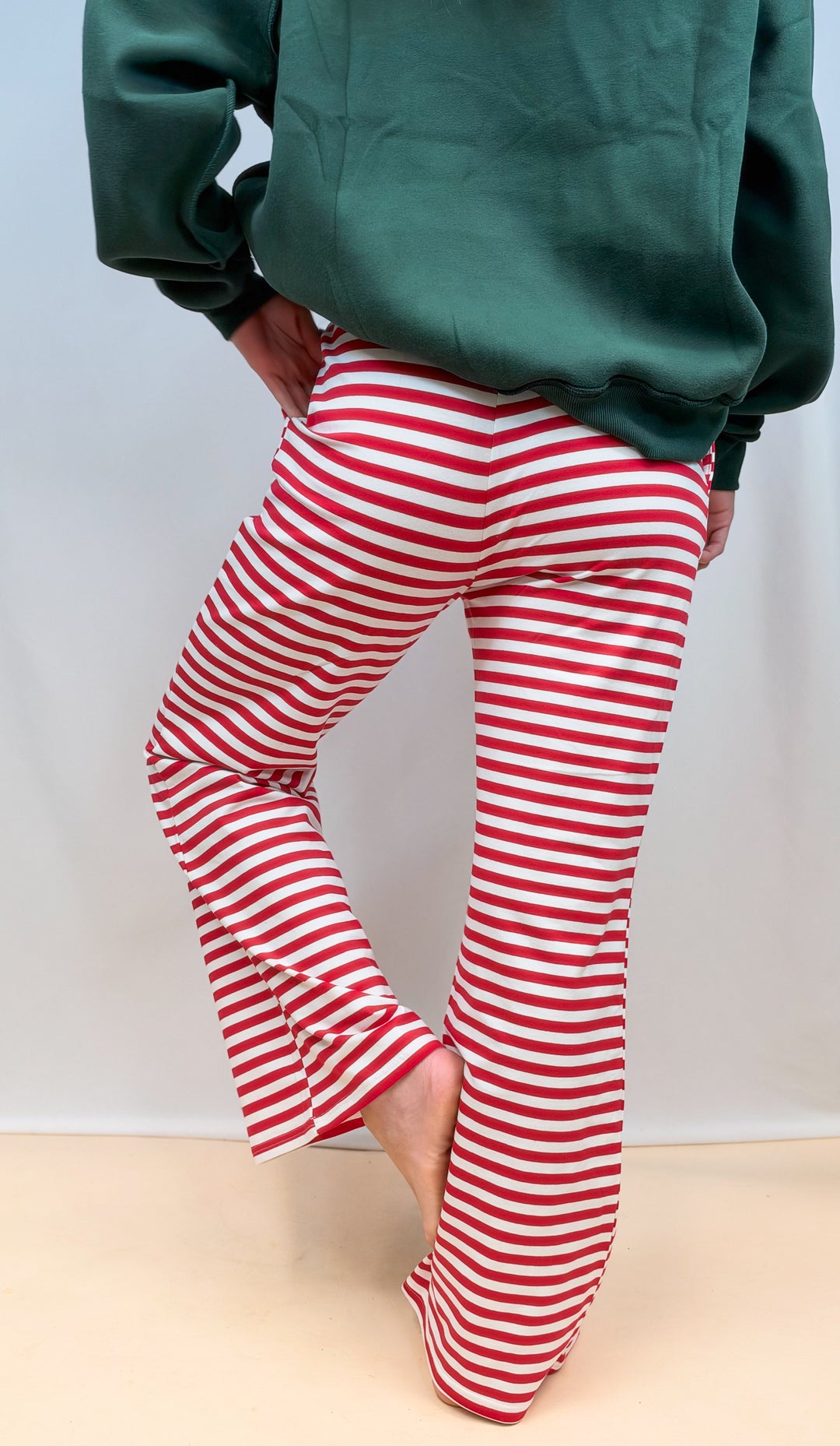 Woman shown from back wearing green sweatshirt wearing red and white stripe pants on plain background