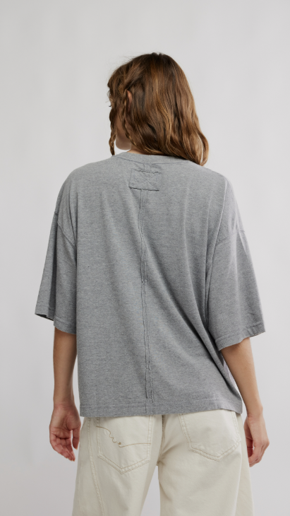 Back of woman wearing grey oversized tee and beige pants on white background