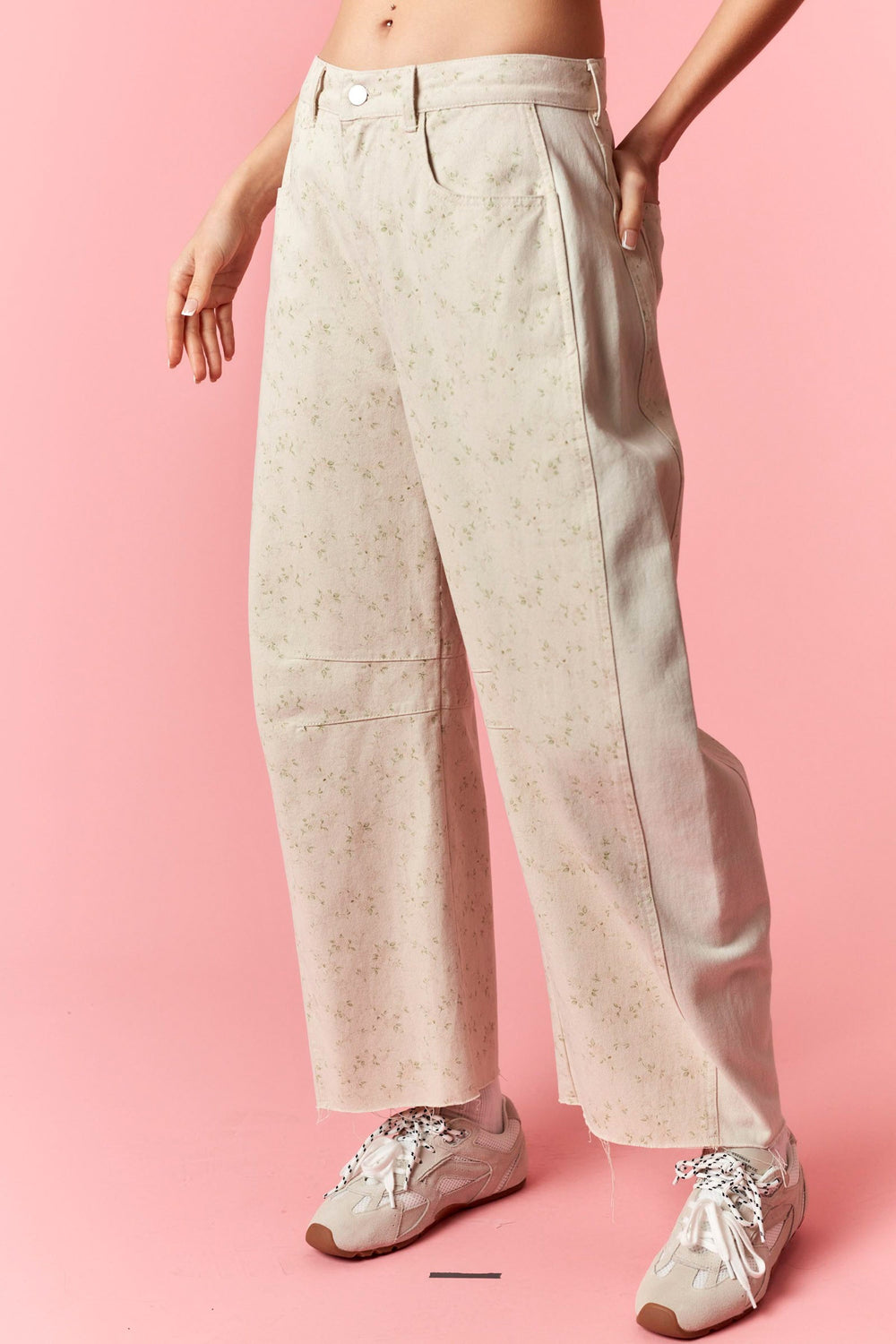 Person wearing light-colored pants and white sneakers on a pink background