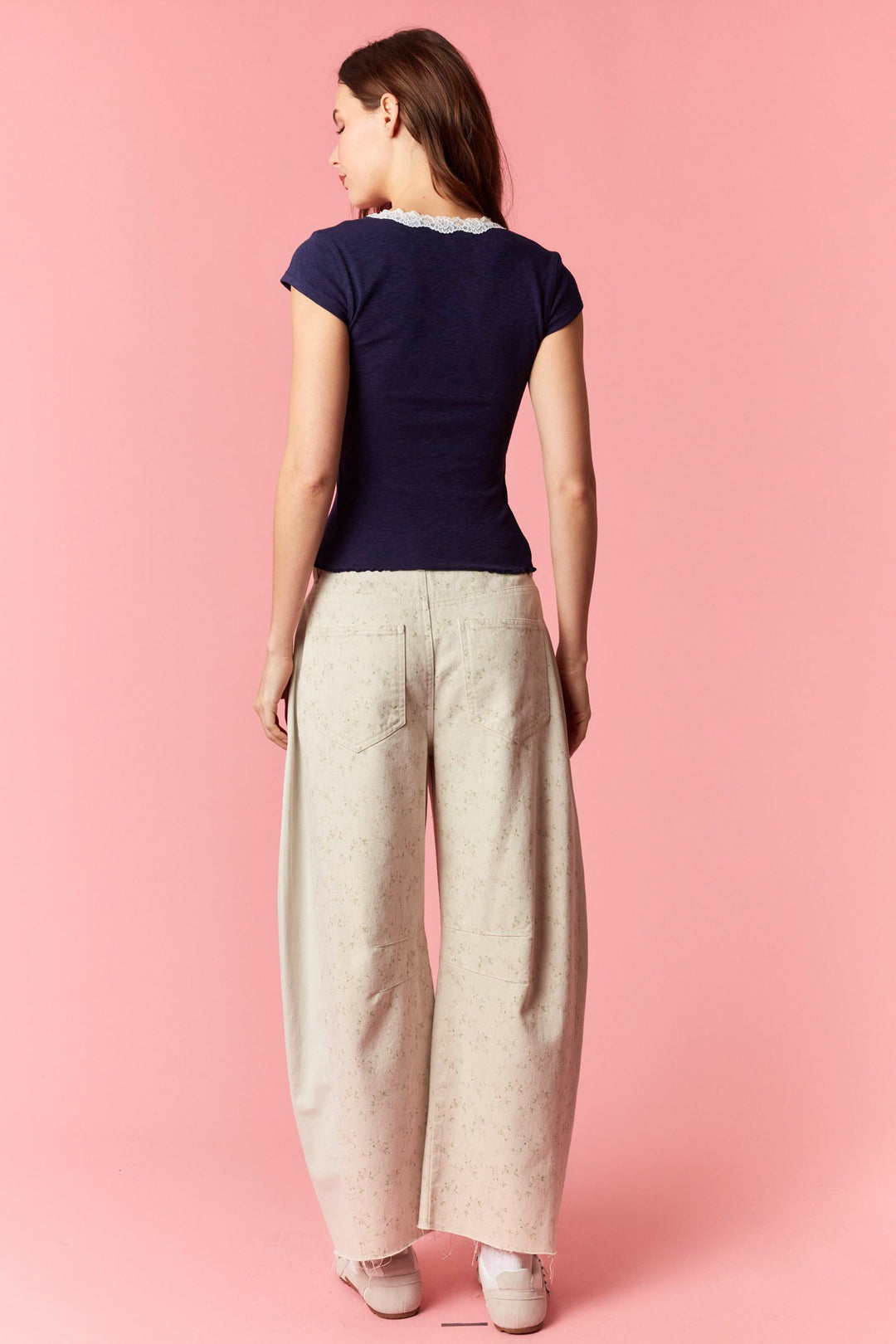 Woman wearing a navy blue top and beige pants on a pink background