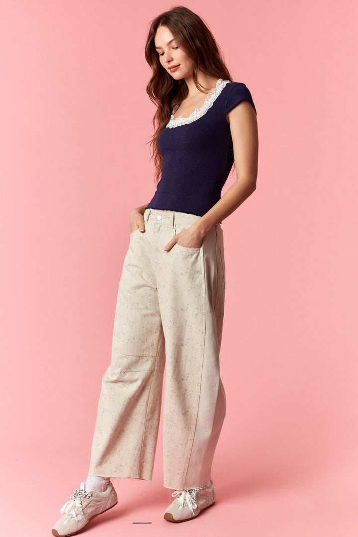 Woman wearing a navy top and beige pants on a pink background
