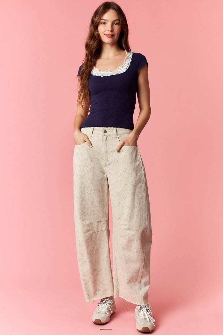Woman wearing a navy top with lace trim and beige wide-leg pants on a pink background