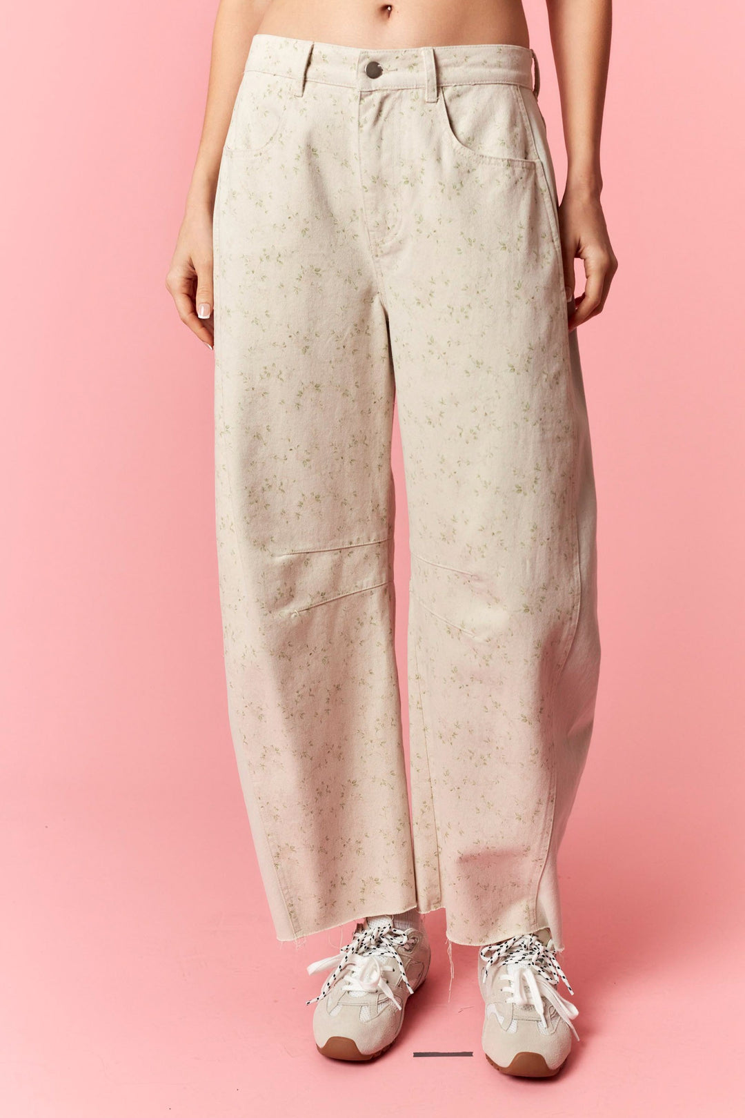 Person wearing light-colored pants and white sneakers on a pink background
