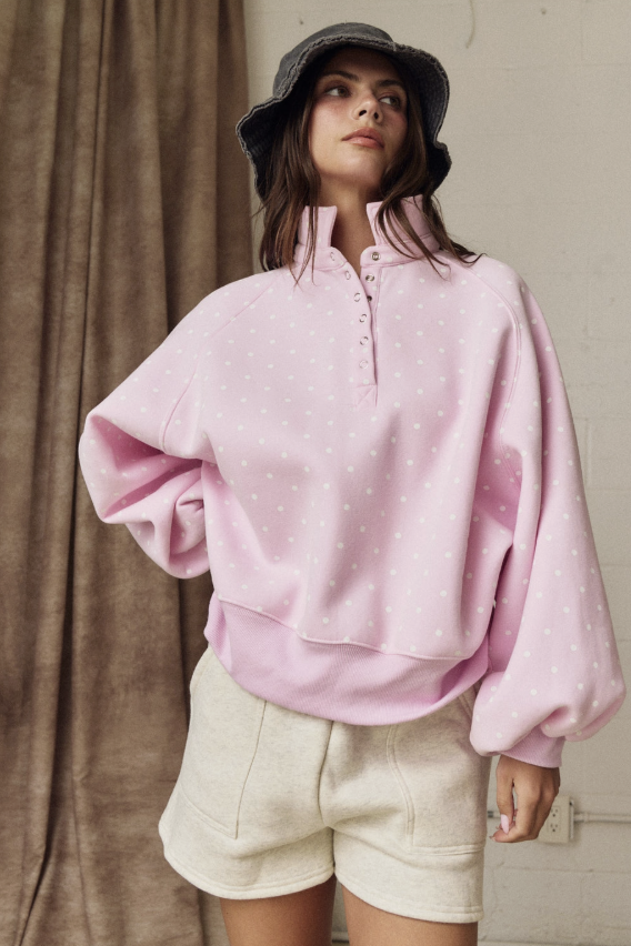 Person wearing a pink sweater and beige shorts against a neutral background