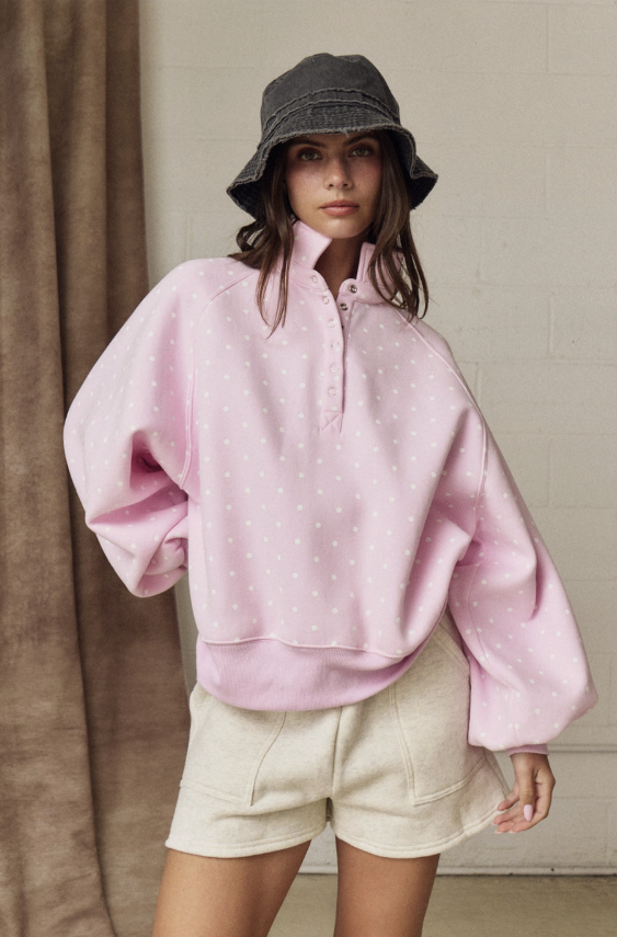 Person wearing a pink oversized shirt and beige shorts with a gray bucket hat indoors.