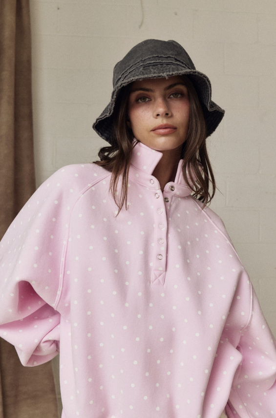 Person wearing a pink polka dot shirt and gray bucket hat against a neutral background