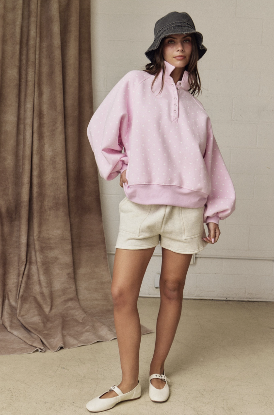 Person wearing a pink oversized hoodie, white shorts, and a black bucket hat against a neutral background.