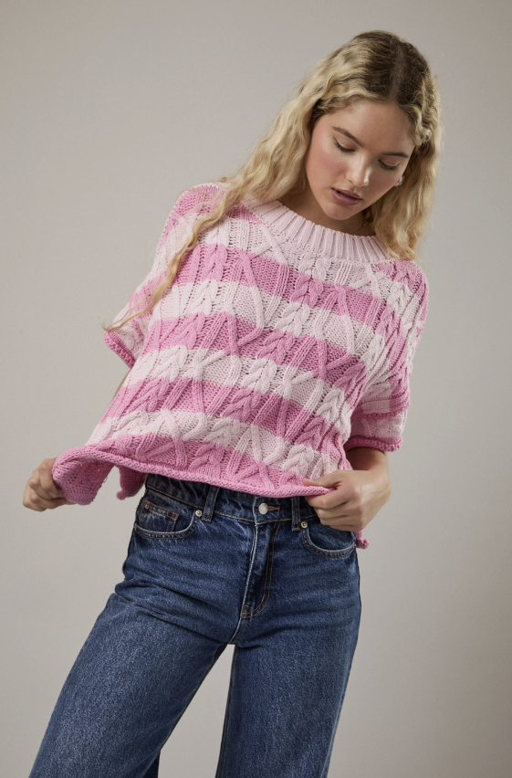 Woman wearing a pink and white striped sweater and blue jeans on a plain background