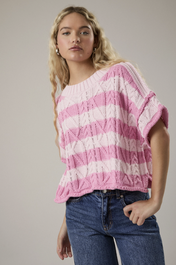 Woman wearing a pink and white striped sweater with blue jeans on a plain background