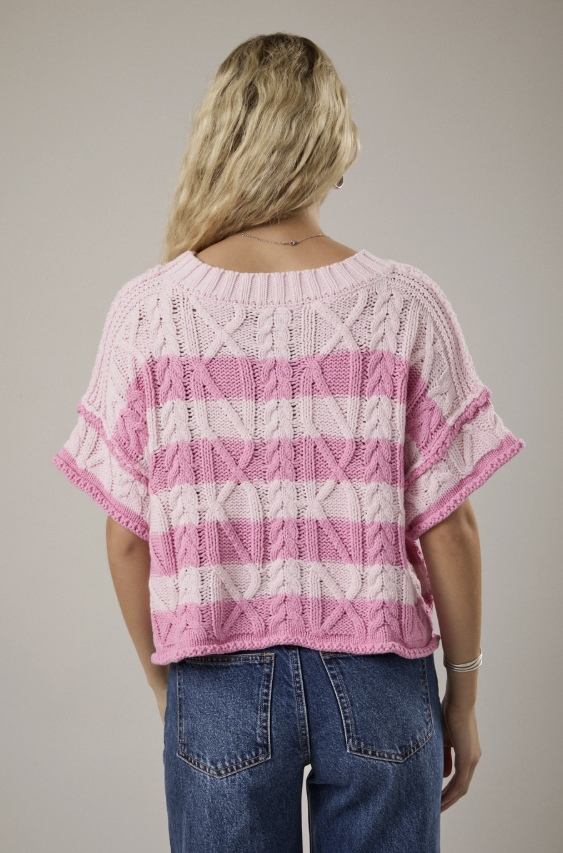 Person wearing a pink and white patterned sweater with blue jeans on a plain background