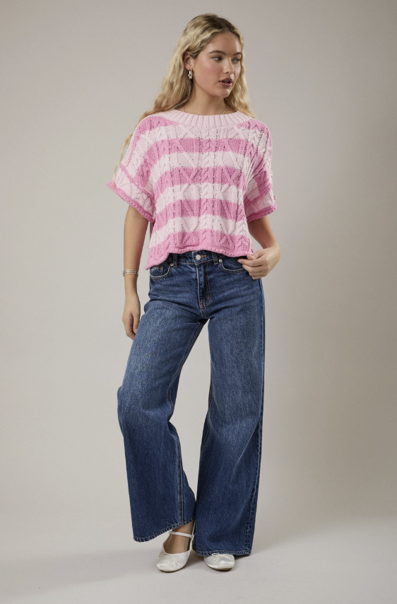Woman wearing a pink and white striped top and blue jeans against a plain background