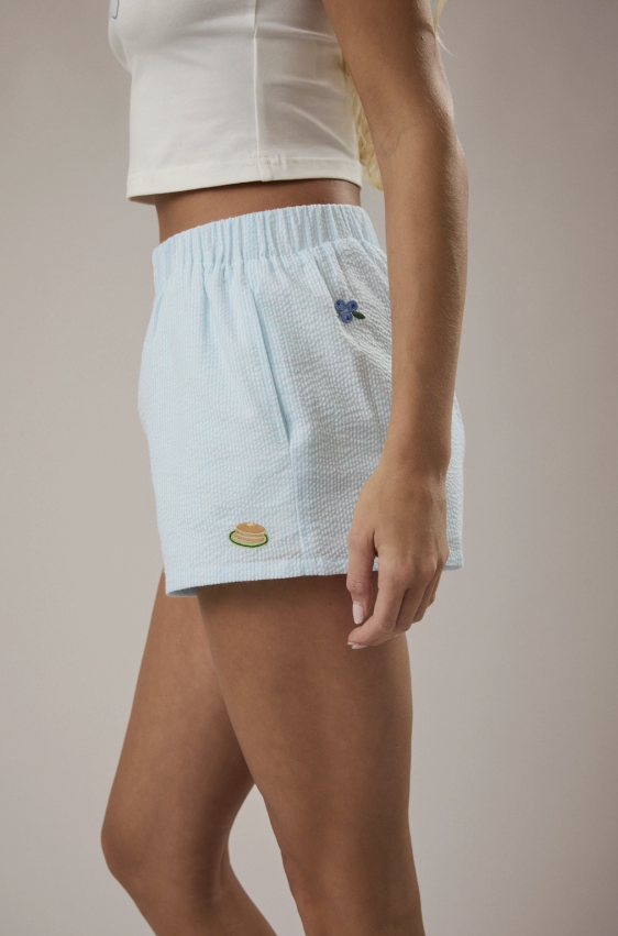 Light blue athletic shorts with embroidered designs on a neutral background