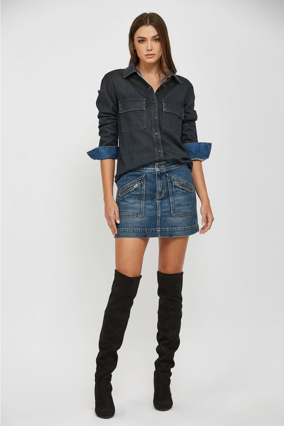 Woman wearing a dark denim shirt, denim skirt, and black knee-high boots on a white background