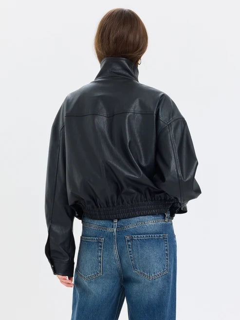 A model shown from the back wearing a black faux-leather jacket and blue jeans against a plain white studio background.