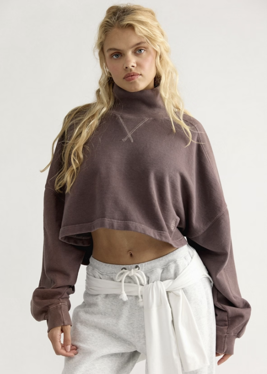 Woman wearing brown mock neck sweatshirt with grey sweatpants on white background