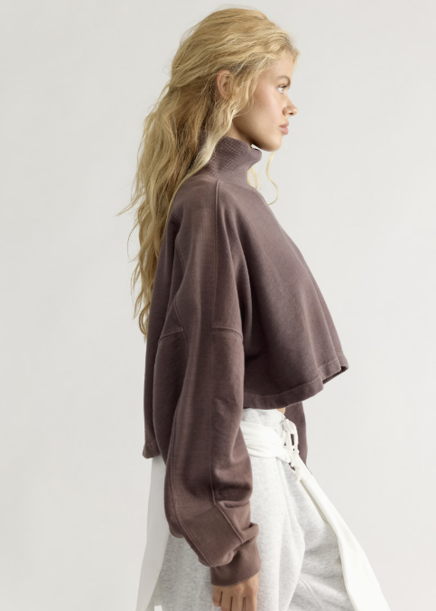 Woman wearing brown mock neck sweatshirt with grey sweatpants on white background