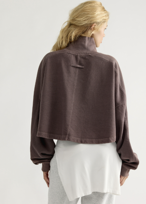 Woman shown from back wearing brown mock neck sweatshirt with grey sweatpants on white background