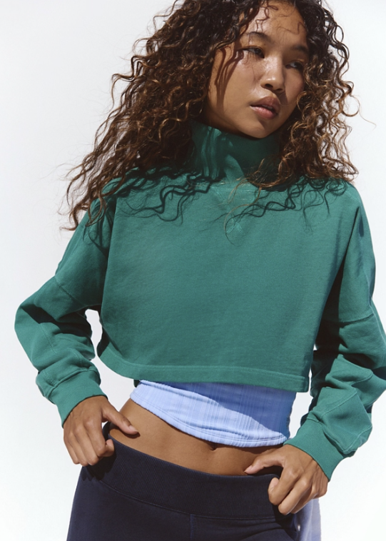 Woman wearing green mock neck sweatshirt and black pants on white background