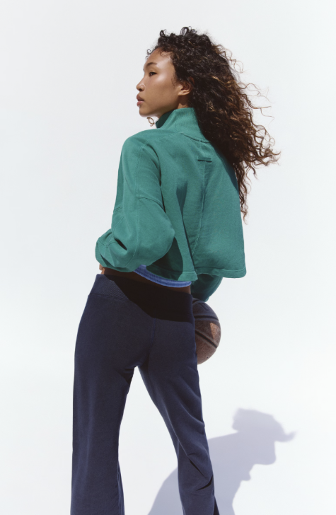 Woman shown from back wearing green mock neck sweatshirt and black pants on white background