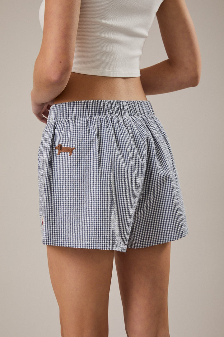 Person wearing a white crop top and blue checkered shorts on a beige background