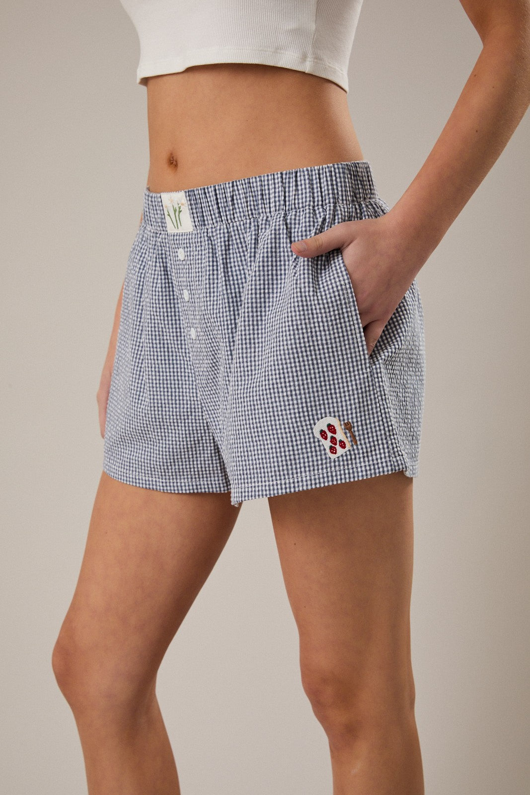 Person wearing blue checkered shorts with a small logo on a neutral background