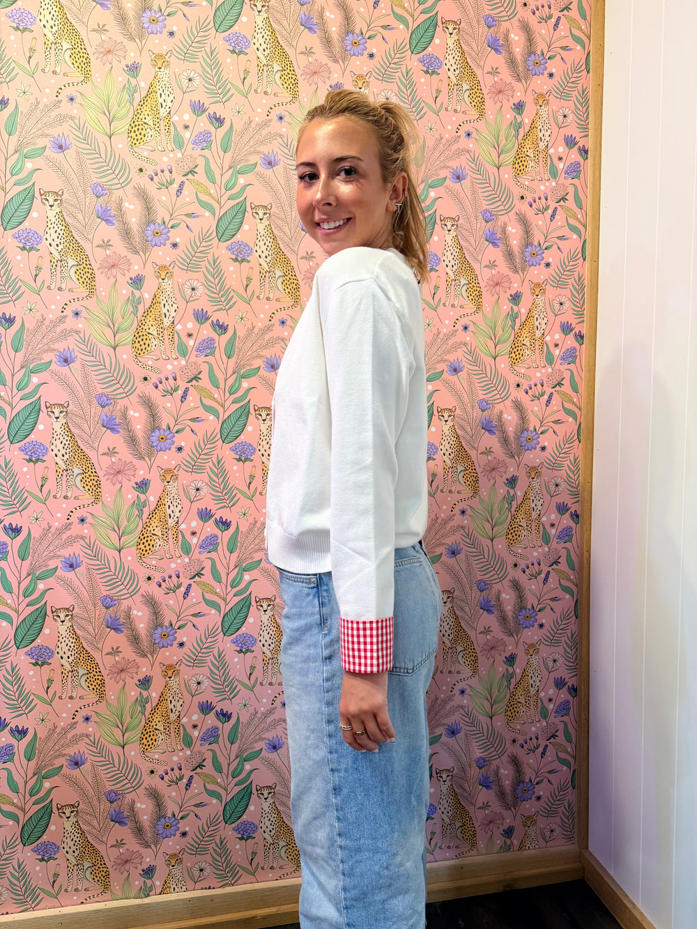 Woman wearing white cardigan with red and white gingham trim on floral background