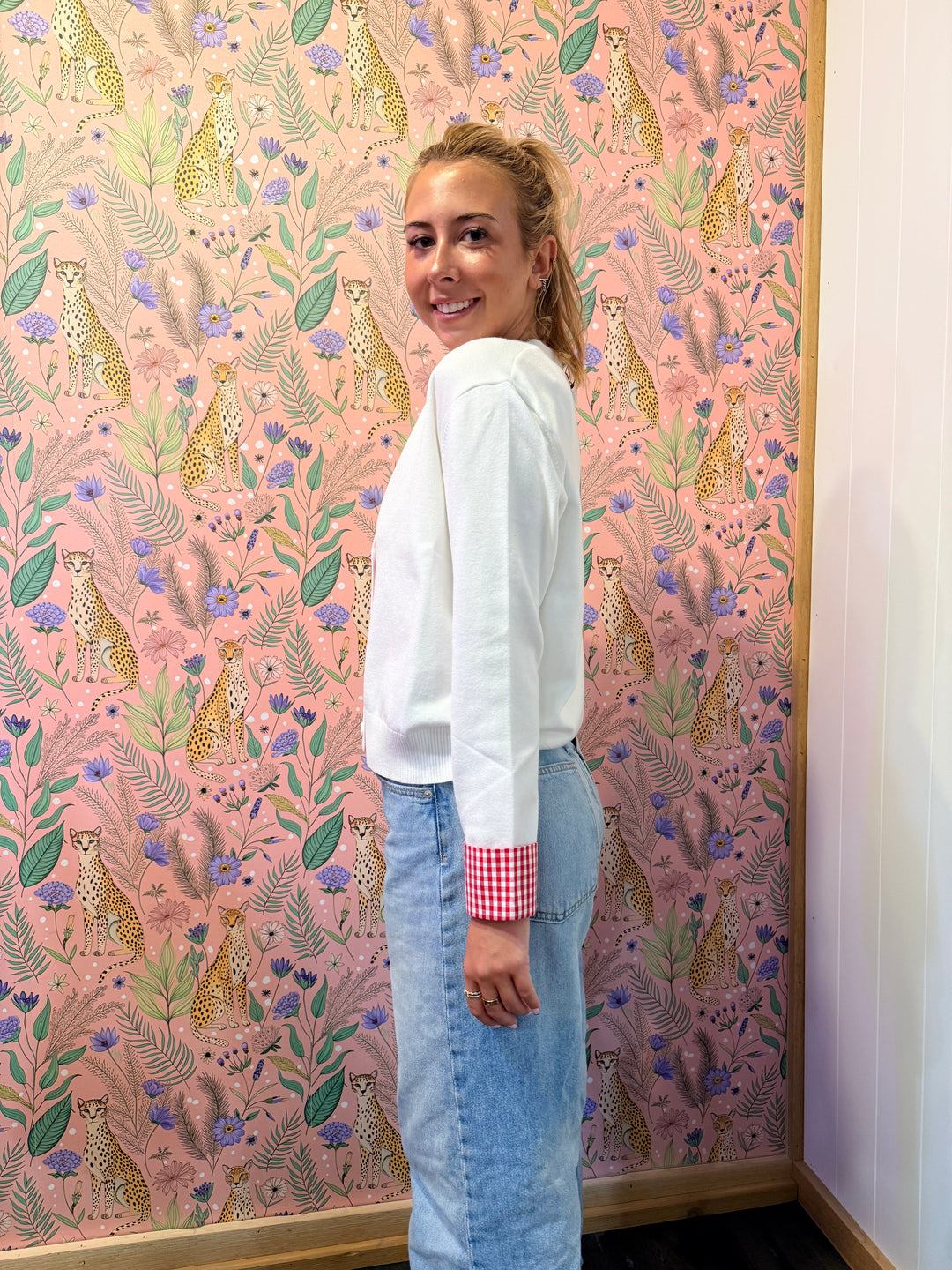 Woman wearing white cardigan with red and white gingham trim on floral background