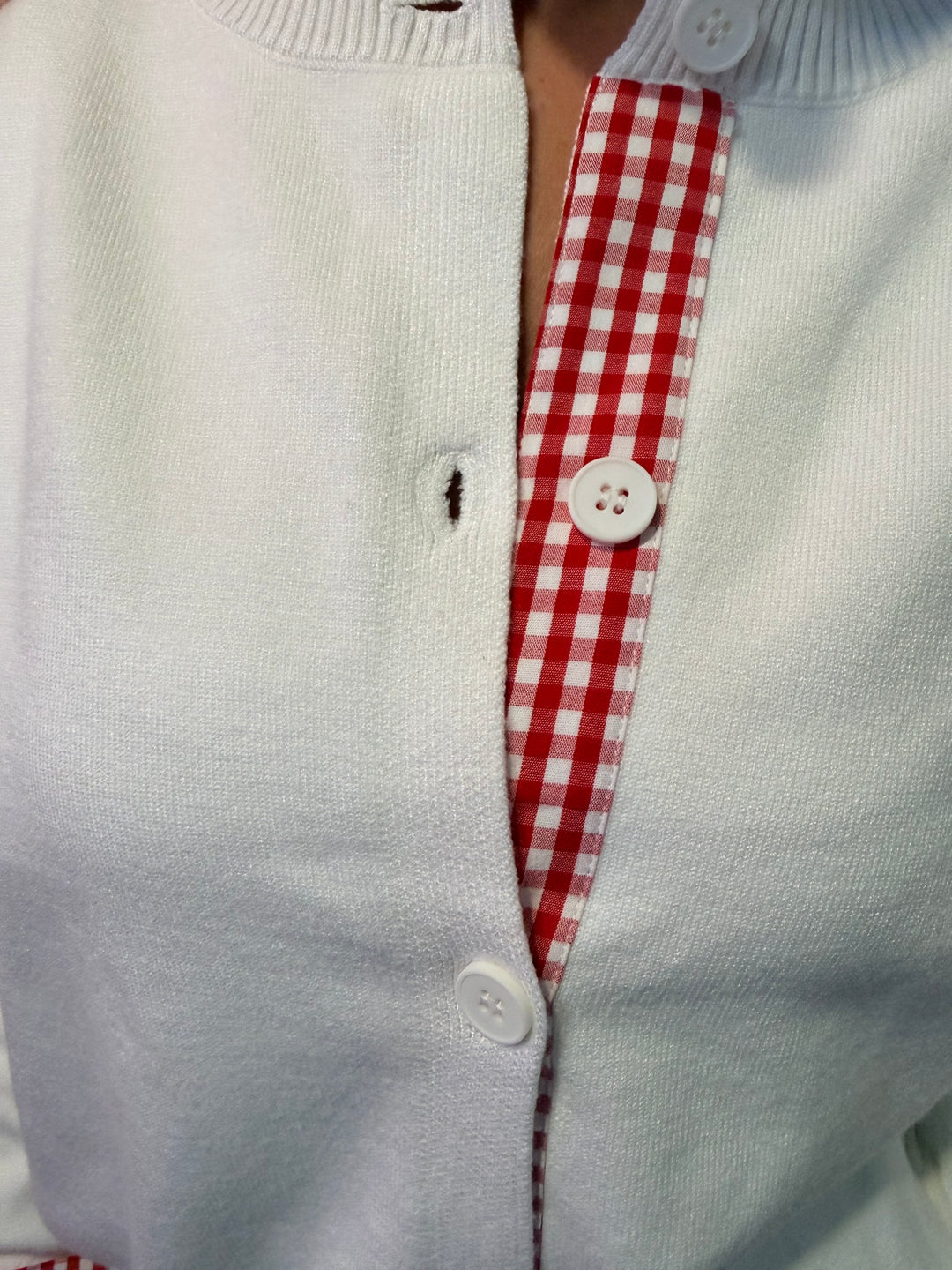Close up of white cardigan with red and white gingham trim