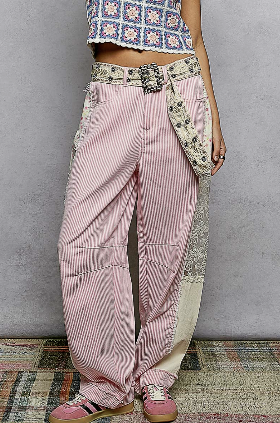 Person wearing pink striped pants with decorative patches against a gray wall.