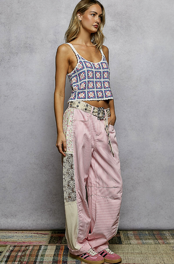 Woman wearing a patterned top and pink pants against a gray wall.