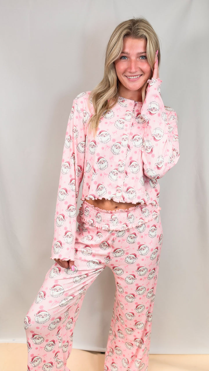 Woman wearing pink christmas pajamas with vintage santa faces and bows on plain background