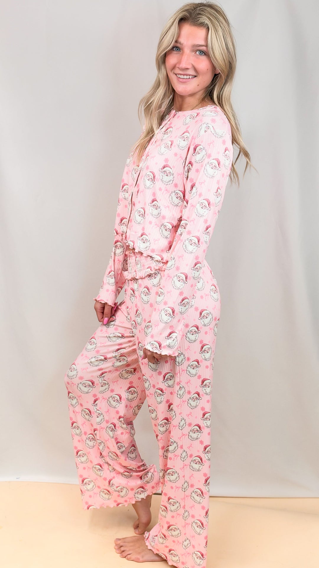 Woman wearing pink christmas pajamas with vintage santa faces and bows on plain background