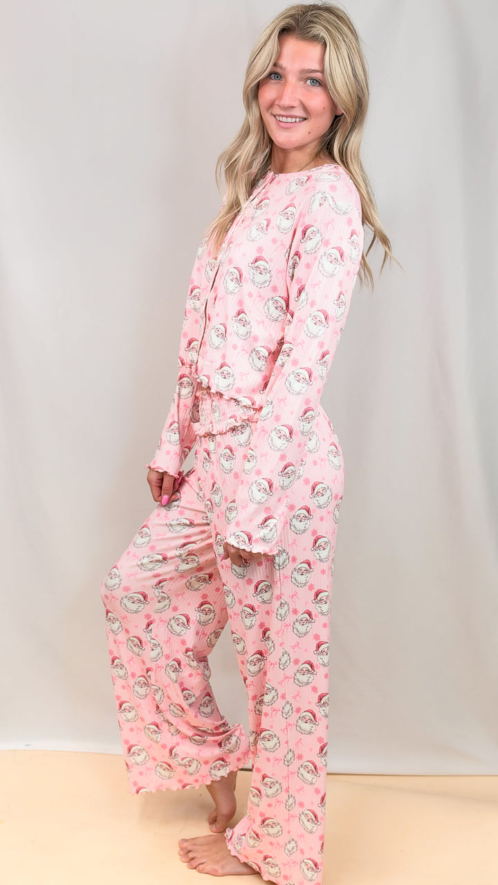 Woman wearing pink christmas pajamas with vintage santa faces and bows on plain background