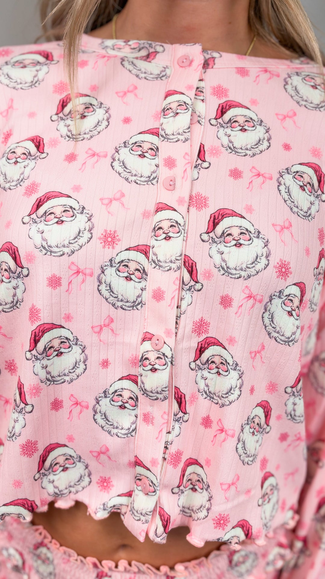Close up of woman wearing pink christmas pajamas with vintage santa faces and bows on plain background