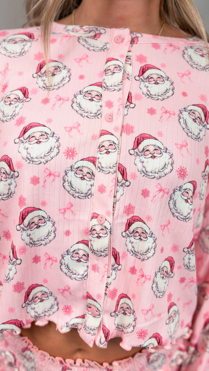 Close up of woman wearing pink christmas pajamas with vintage santa faces and bows on plain background