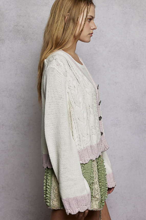 Woman wearing white cardigan with pink trim on plain background