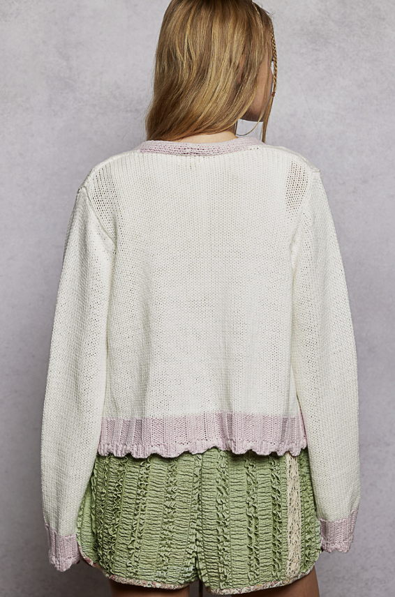 Woman wearing white cardigan with pink trim on plain background