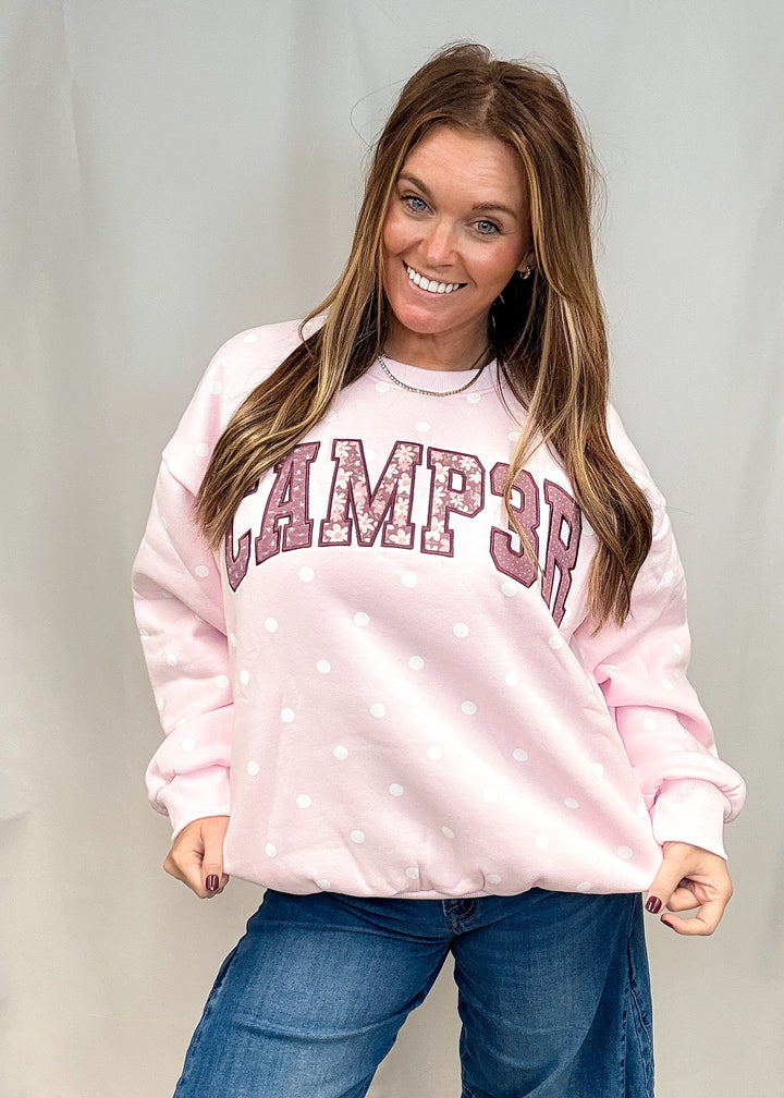 A woman wearing a light pink crewneck sweatshirt with white polka dots and &