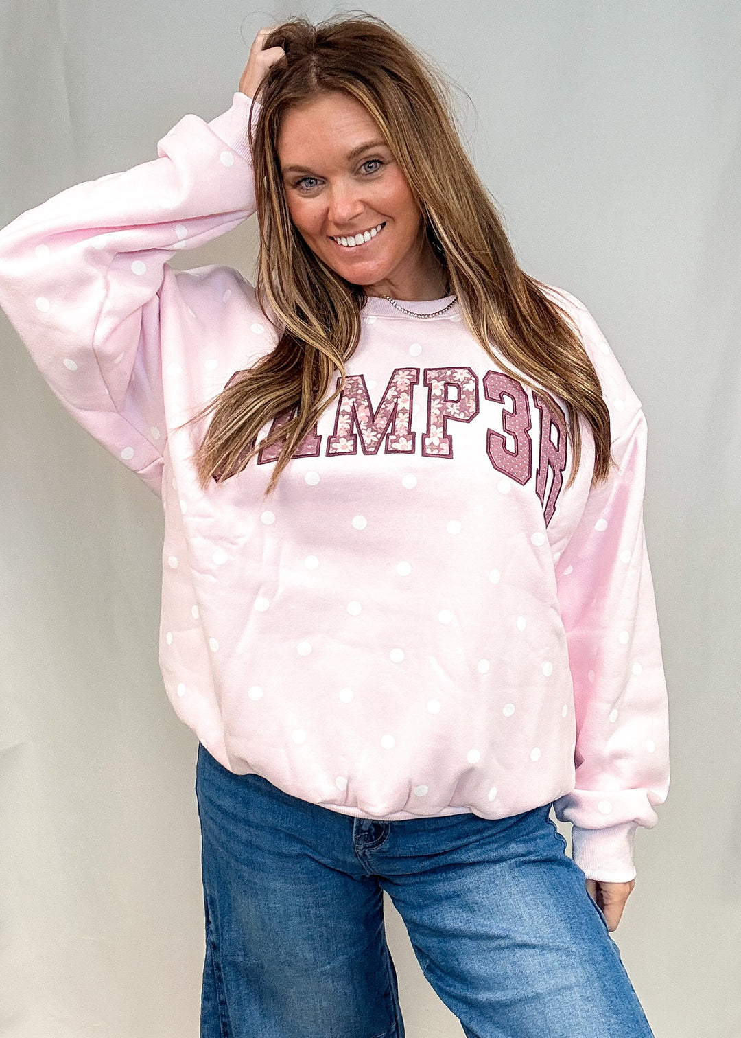A woman modeling a light pink crewneck sweatshirt with white polka dots and &